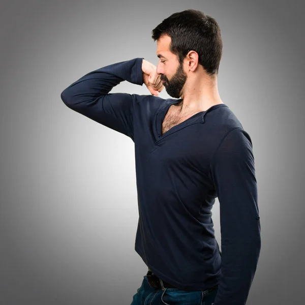 Bonito homem com barba fazendo um gesto forte no fundo cinza — Fotografia de Stock