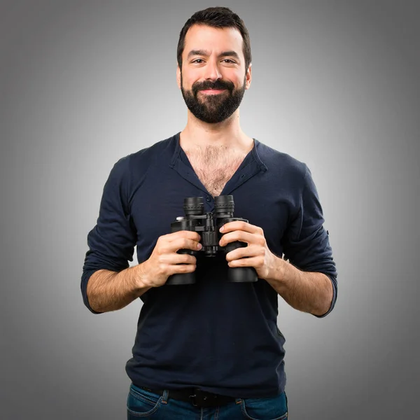 Schöner Mann mit Bart und Fernglas auf grauem Hintergrund — Stockfoto