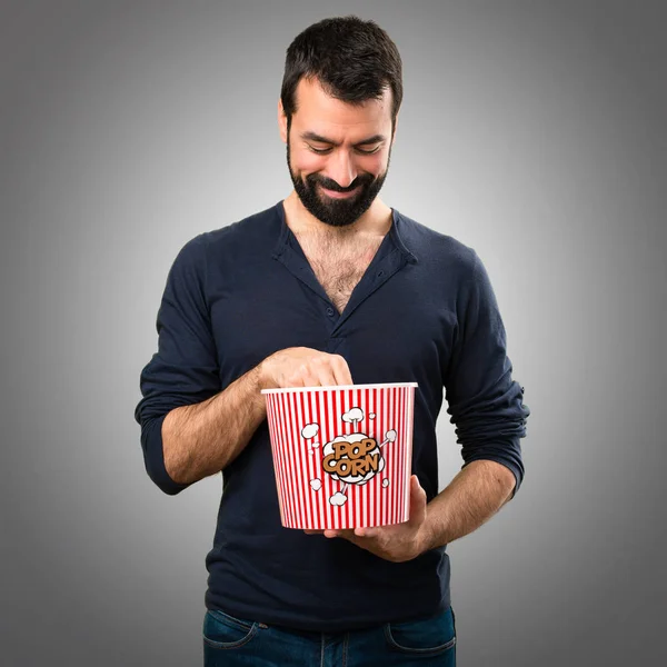 Popcorns gri arka plan üzerinde yemek sakallı yakışıklı adam