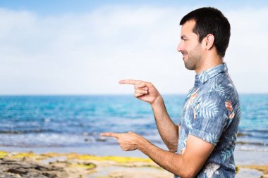 Plajda lateral işaret eden çiçek forması ile yakışıklı adam