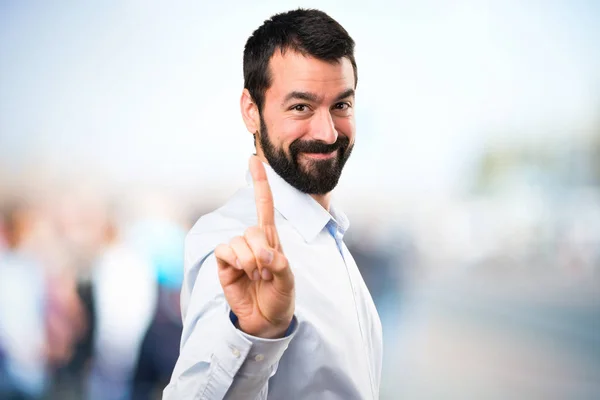 Hombre guapo con barba contando uno sobre fondo desenfocado — Foto de Stock