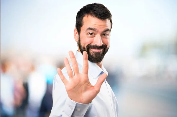 Bonito homem com barba contando cinco com fundo desfocado — Fotografia de Stock