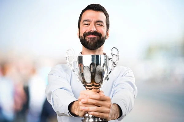 Happy Handsome man with beard holding a trophy on unfocused back — Stock Photo, Image