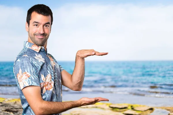 Hombre guapo con camisa de flores sosteniendo algo en la playa —  Fotos de Stock