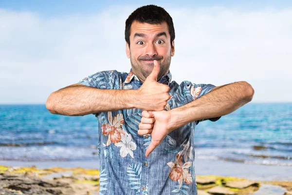 Stilig man med blomma skjorta att göra bra-dåligt tecken på stranden — Stockfoto