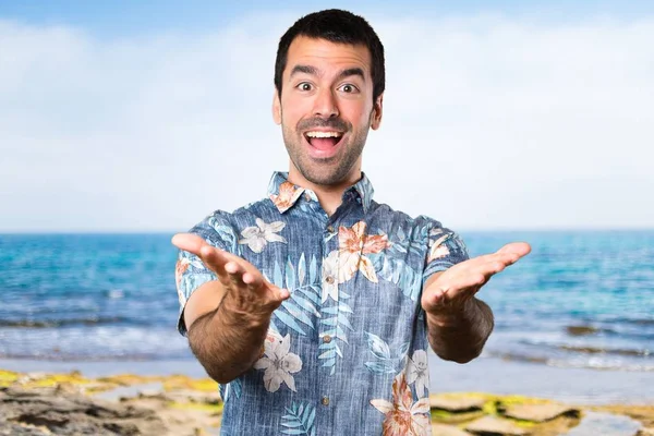 Hombre guapo con camisa de flores presentando algo en la playa —  Fotos de Stock