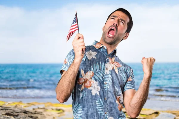 Stilig man med blomma skjorta håller en amerikansk flagga på stranden — Stockfoto