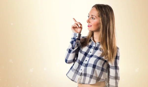Blondes Teenie-Mädchen zeigt auf ockerfarbenen Hintergrund — Stockfoto