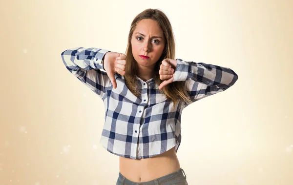 Blonde teen girl making bad signal on ocher background — Stock Photo, Image