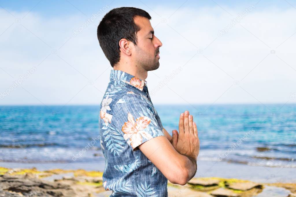 Handsome man with flower shirt in zen position at the beach