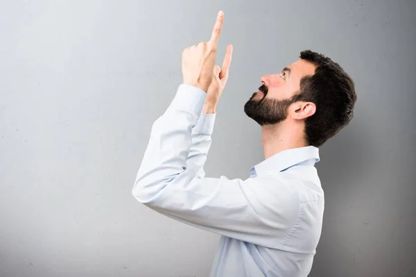 Hombre guapo con barba apuntando hacia arriba sobre fondo texturizado — Foto de Stock