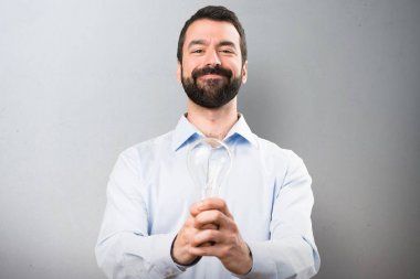 Sakallı bir ampul dokulu arka plan üzerinde tutan mutlu yakışıklı adam