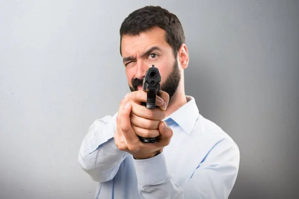 Bonito homem com barba atirando com uma pistola no fundo texturizado — Fotografia de Stock
