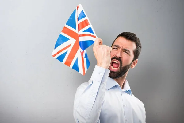 Ευτυχισμένος όμορφος άντρας με γένια, κρατώντας μια σημαία του Ηνωμένου Βασιλείου σε φόντο με υφή — Φωτογραφία Αρχείου