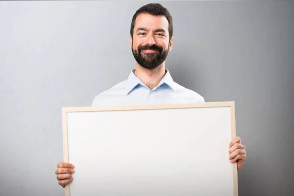 Homem bonito feliz com barba segurando um cartaz vazio no fundo texturizado — Fotografia de Stock