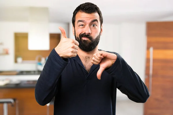 Beau homme avec barbe faisant signe bon-mauvais à l'intérieur de la maison — Photo