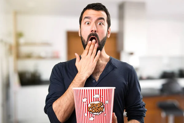 Handsome man with beard eating popcorns inside house