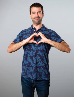 Esmer adam gri arka plan üzerinde elleriyle bir kalp yapma