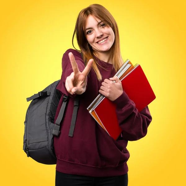 Studentka žena dělat vítězství gesto na barevné pozadí — Stock fotografie