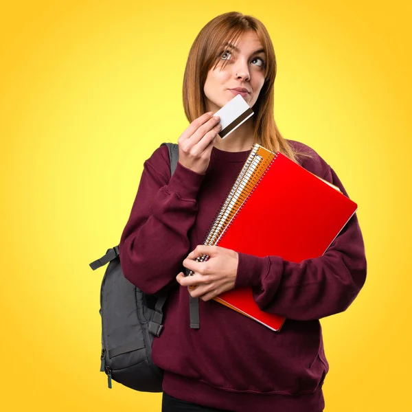 Renkli arka plan üzerinde bir kredi kartı tutan öğrenci kadın