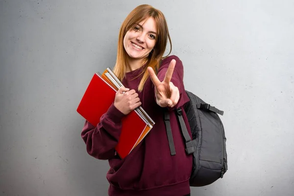 Studerande kvinna gör seger gest på grå bakgrund — Stockfoto