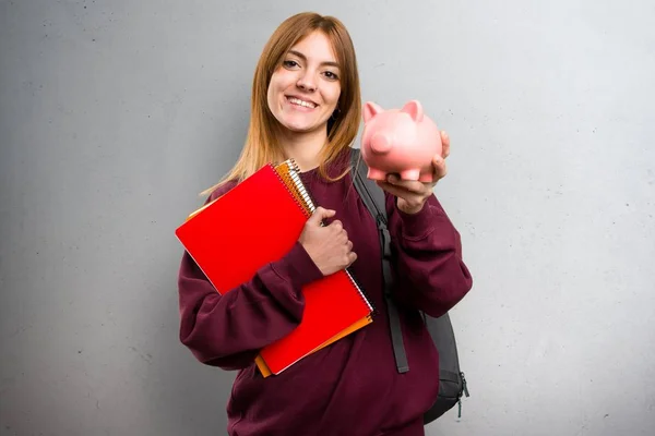 Studentka žena držící prasátko na šedém pozadí — Stock fotografie