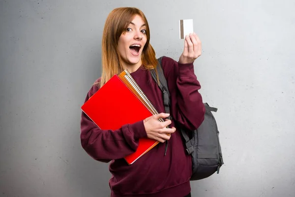 Student woman holding a credit card on grey background