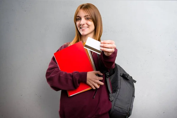 Mulher estudante segurando um cartão de crédito em fundo cinza — Fotografia de Stock