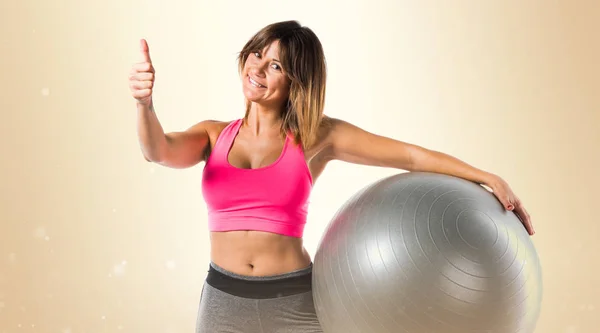 Sport vrouw met fit-bal en met duim omhoog op okergeel achtergrond — Stockfoto