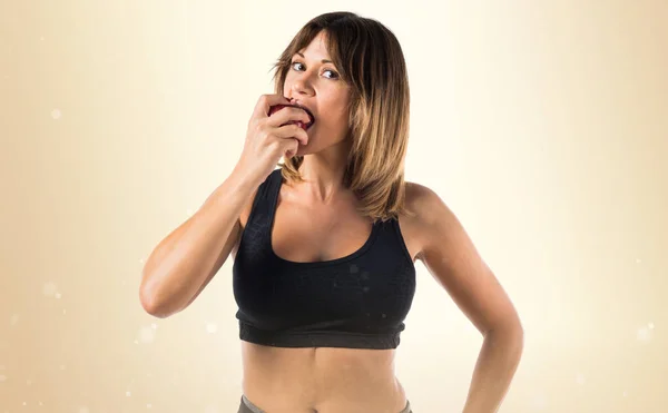 Sport woman eating an apple on ocher background — Stock Photo, Image
