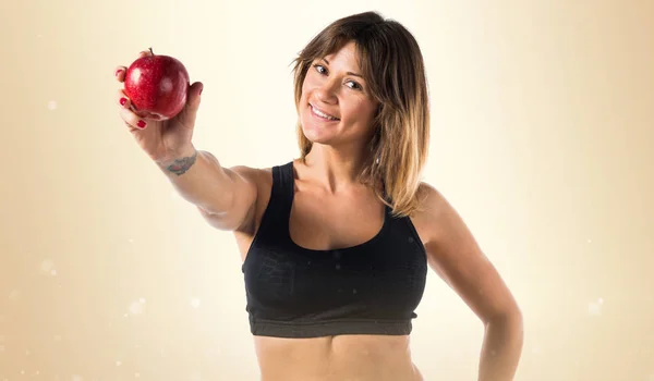 Deporte mujer mostrando una manzana en ocre fondo —  Fotos de Stock