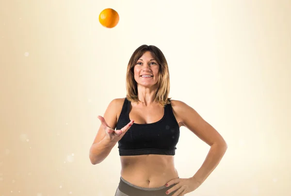 Deporte mujer jugando con un naranja sobre fondo ocre —  Fotos de Stock