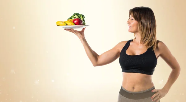 Sport vrouw met fruit en groenten op okergeel achtergrond — Stockfoto