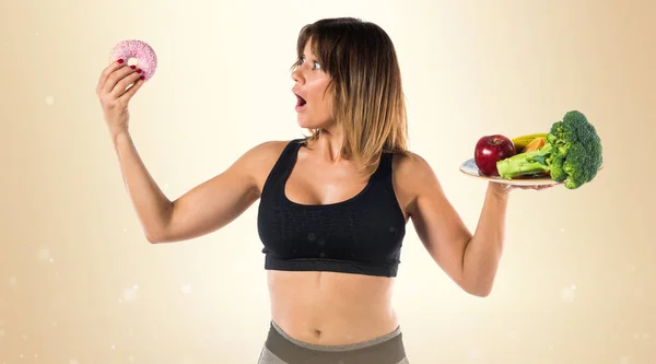 Esporte mulher segurando frutas e legumes em uma mão e donut — Fotografia de Stock