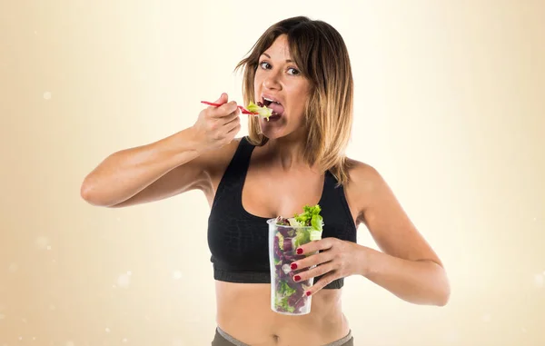 Hübsche Sportlerin mit Salat auf ockerfarbenem Hintergrund — Stockfoto