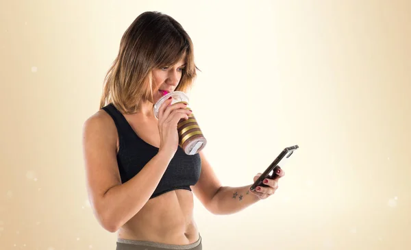Sport donna con il suo cellulare e bere una bevanda sportiva su ocra — Foto Stock