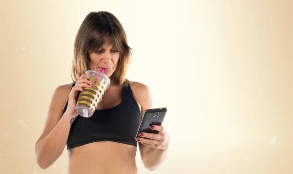 Femme sportive avec son mobile et boire une boisson sportive sur ocre — Photo