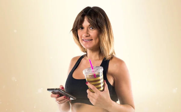 Sportlerin mit Handy und Sportgetränk auf ockerfarbenem Rücken — Stockfoto