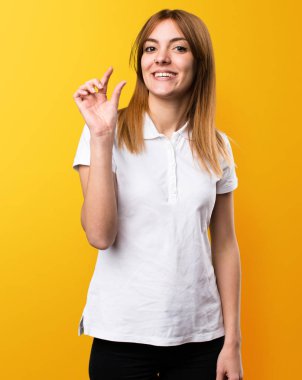 Güzel genç kız küçük işareti üzerinde sarı arka plan yapma