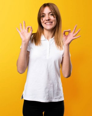 Güzel genç kız sarı arka plan üzerinde oturum Tamam yapma