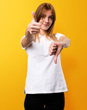 Güzel genç kız iyi-kötü işareti üzerinde sarı arka plan yapma