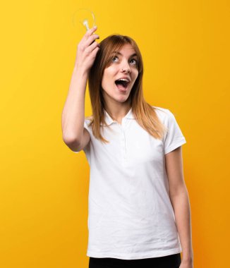 Bir ampul üzerinde sarı backgrou tutan sürpriz güzel genç kız