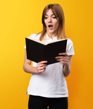 Sürpriz güzel genç kız sarı zemin üzerine kitap okuma