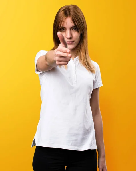 Krásná mladá dívka dělat zbraň gesto na žlutém podkladu — Stock fotografie
