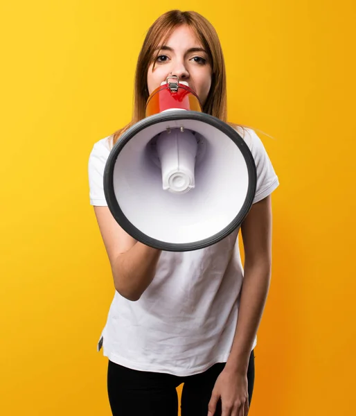 Beautiful young girl holding a megaphone on yellow background — Stock Photo, Image