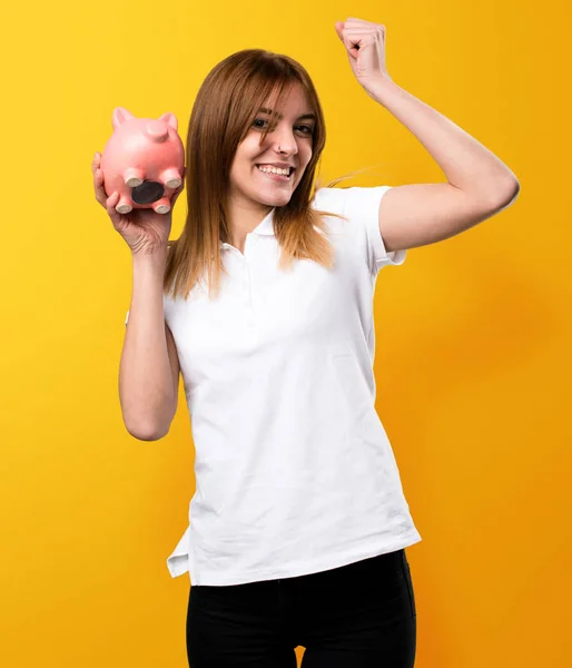 Glücklich schöne junge Mädchen hält ein Sparschwein auf gelbem Backgro — Stockfoto