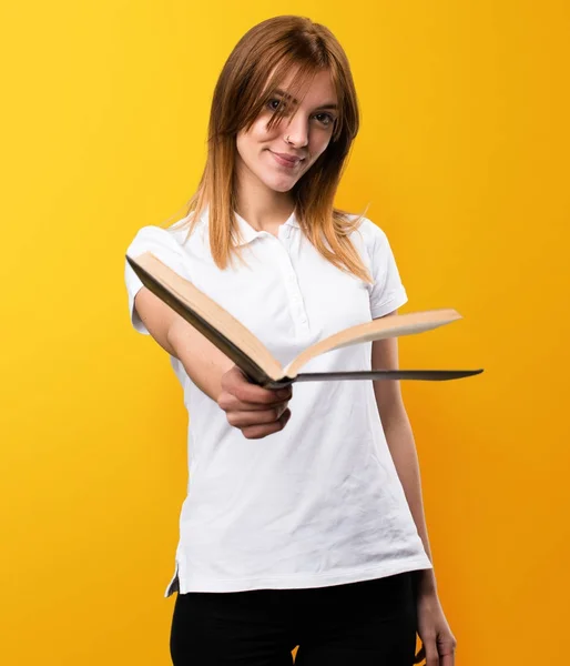 Beautiful young girl reading book on yellow background — Stock Photo, Image