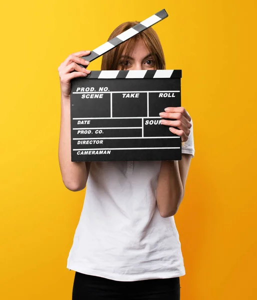 Gadis muda yang cantik memegang clapperboard dengan latar belakang kuning — Stok Foto