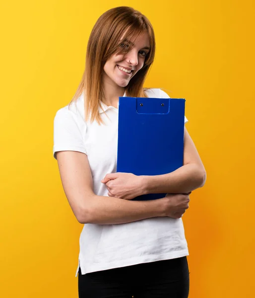 Glad vacker ung flicka håller en mapp på gul bakgrund — Stockfoto