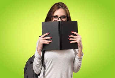 Renkli arka plan ile ilgili bir kitap arkasına saklanmış öğrenci kadın